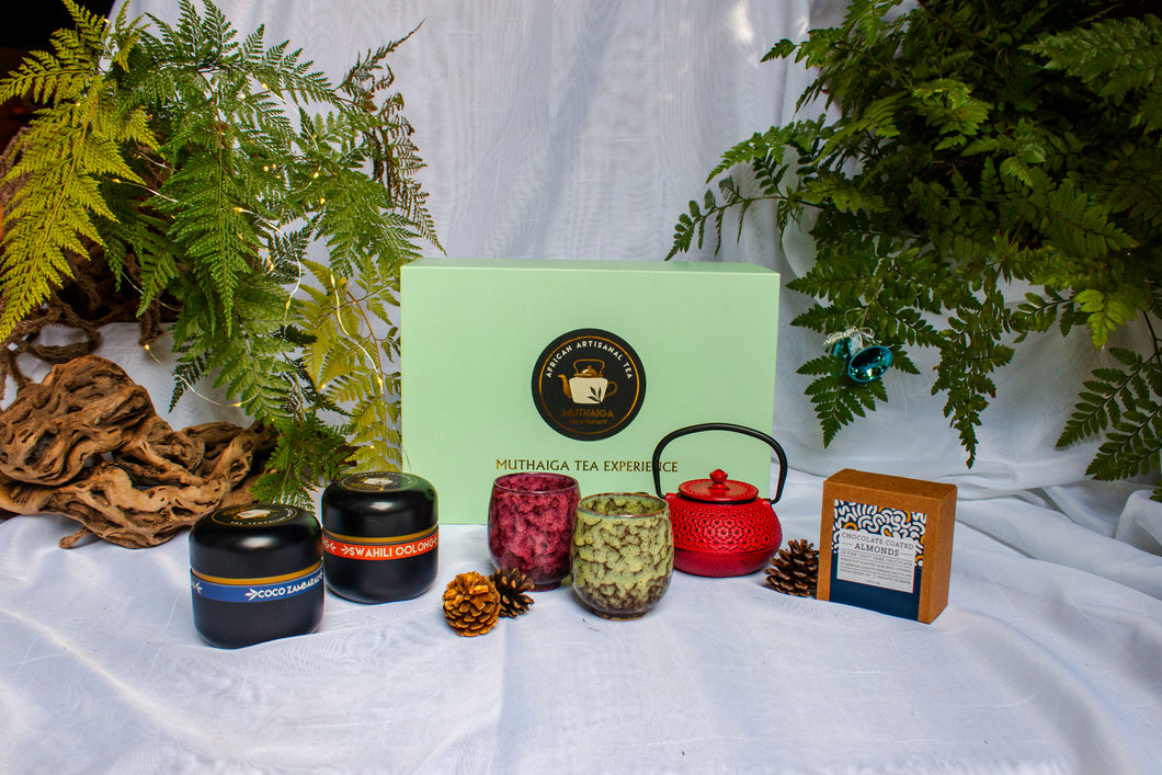 Luxury Christmas gift in Nairobi showcasing a Tea-making set with teapot, tea leaves, and packaging on a white fabric background with plants.