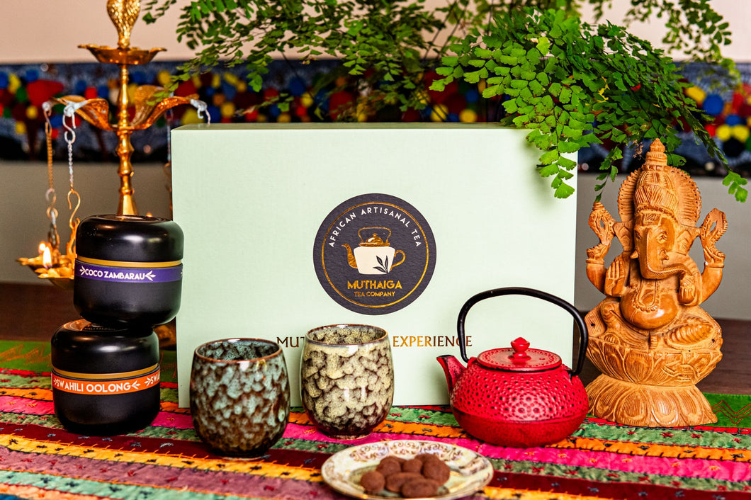 A Luxury Diwali Gift Hamper including a tea pot, candle, and statue on a colorful mat with a branded box in the background.