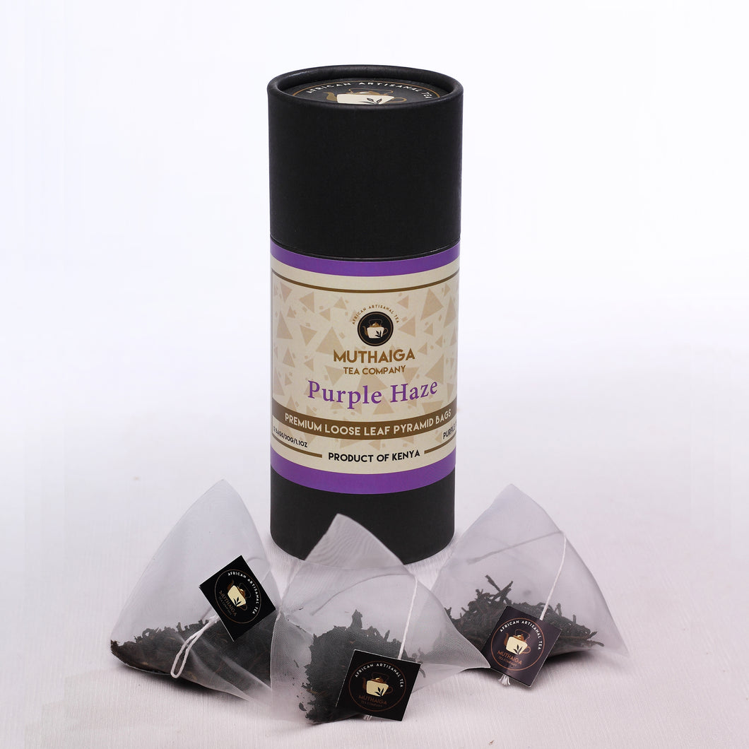 A cylindrical black package labeled 'MUTHAIGA PURPLE HAZE' with purple accents, alongside three clear premium purple tea bags with purple tags.