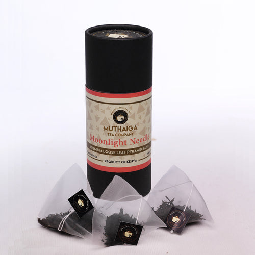 Product packaging for Muthaiga Moonlight Needle white silver tips tea in Kenya, featuring handcrafted loose leaf tea bags and a cylindrical black package with the brand and product name.